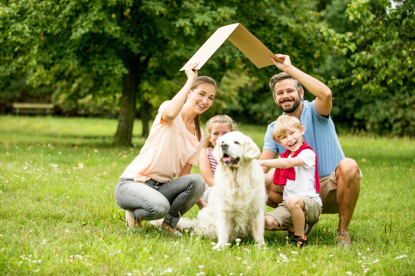 A happy family with two small children and their white Retriever in the park.